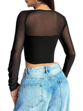 Person wearing a black sheer long-sleeve top and blue jeans against a white wall.