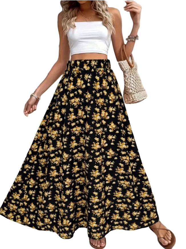 Woman wearing a white top and black floral skirt with a plant and woven bag in the background.
