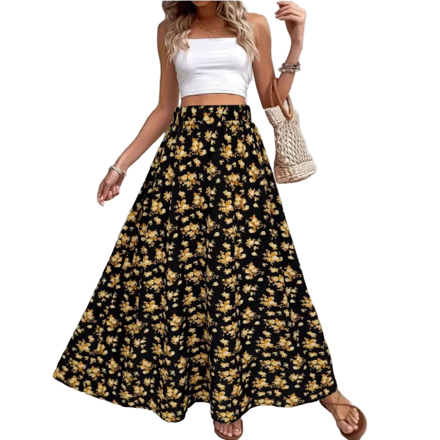 Woman wearing a white top and black floral skirt with a woven bag, standing against a light gray wall.