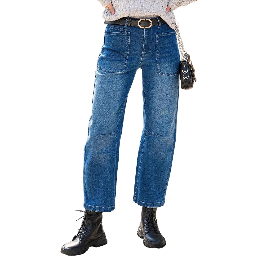 Person wearing blue jeans and black boots standing on a sidewalk.