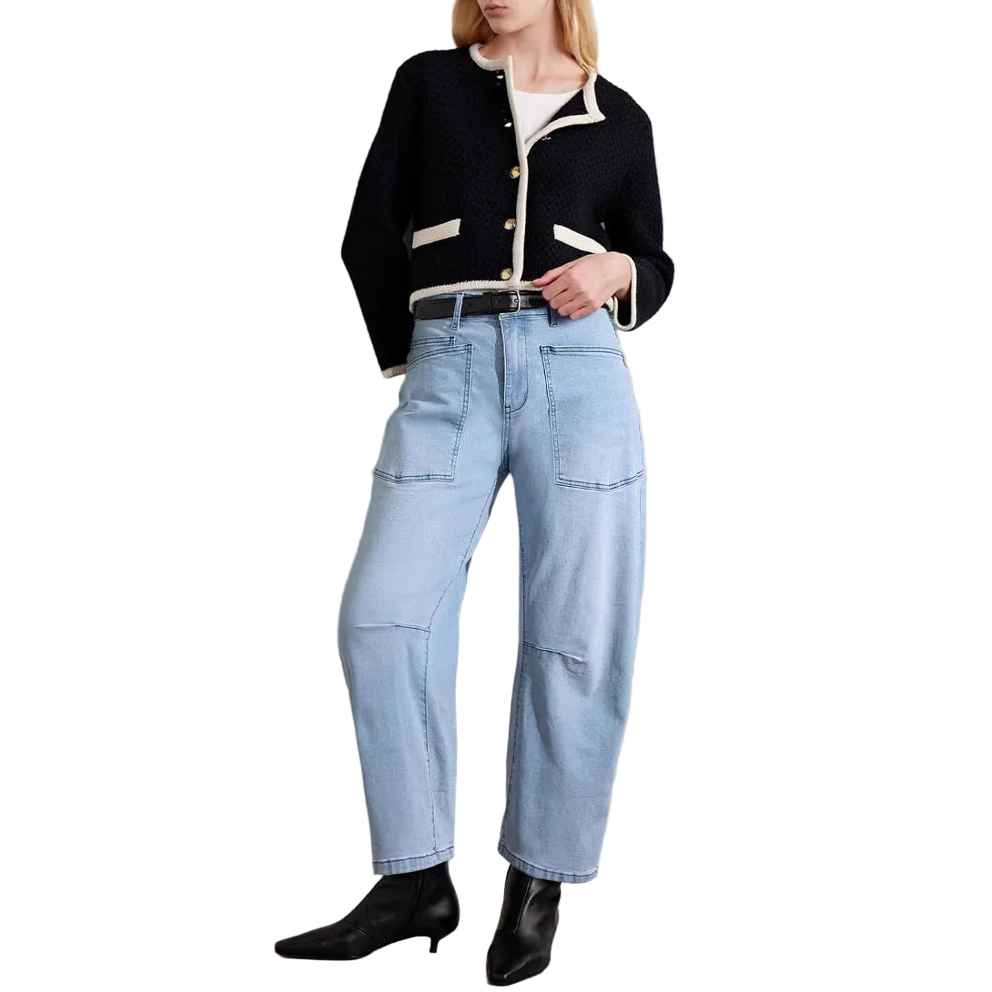 Person wearing a black jacket, white shirt, light blue jeans, and black shoes against a plain background