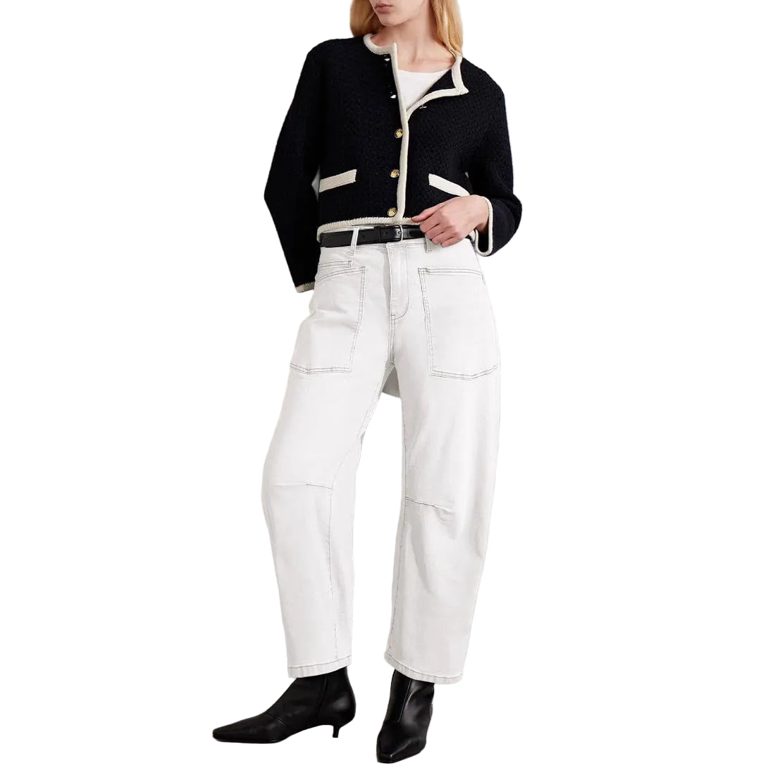 Person wearing a black jacket, white pants, and black shoes against a plain background