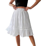 Person wearing a white skirt with lace trim in a minimal indoor setting.