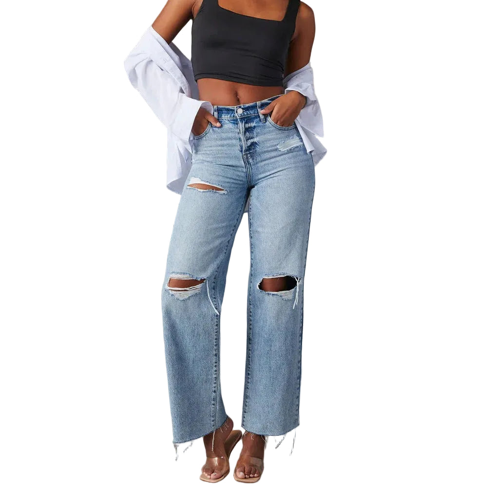 Person wearing ripped blue jeans and a black crop top on a gray background
