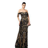 Woman wearing a black and gold evening gown with intricate designs on a white background