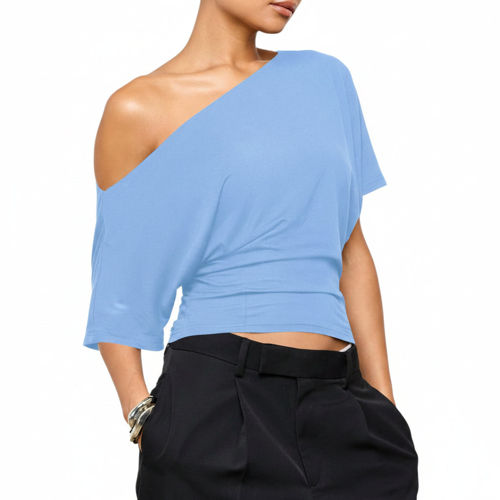 Woman wearing a light blue one-shoulder top and black pants on a white background