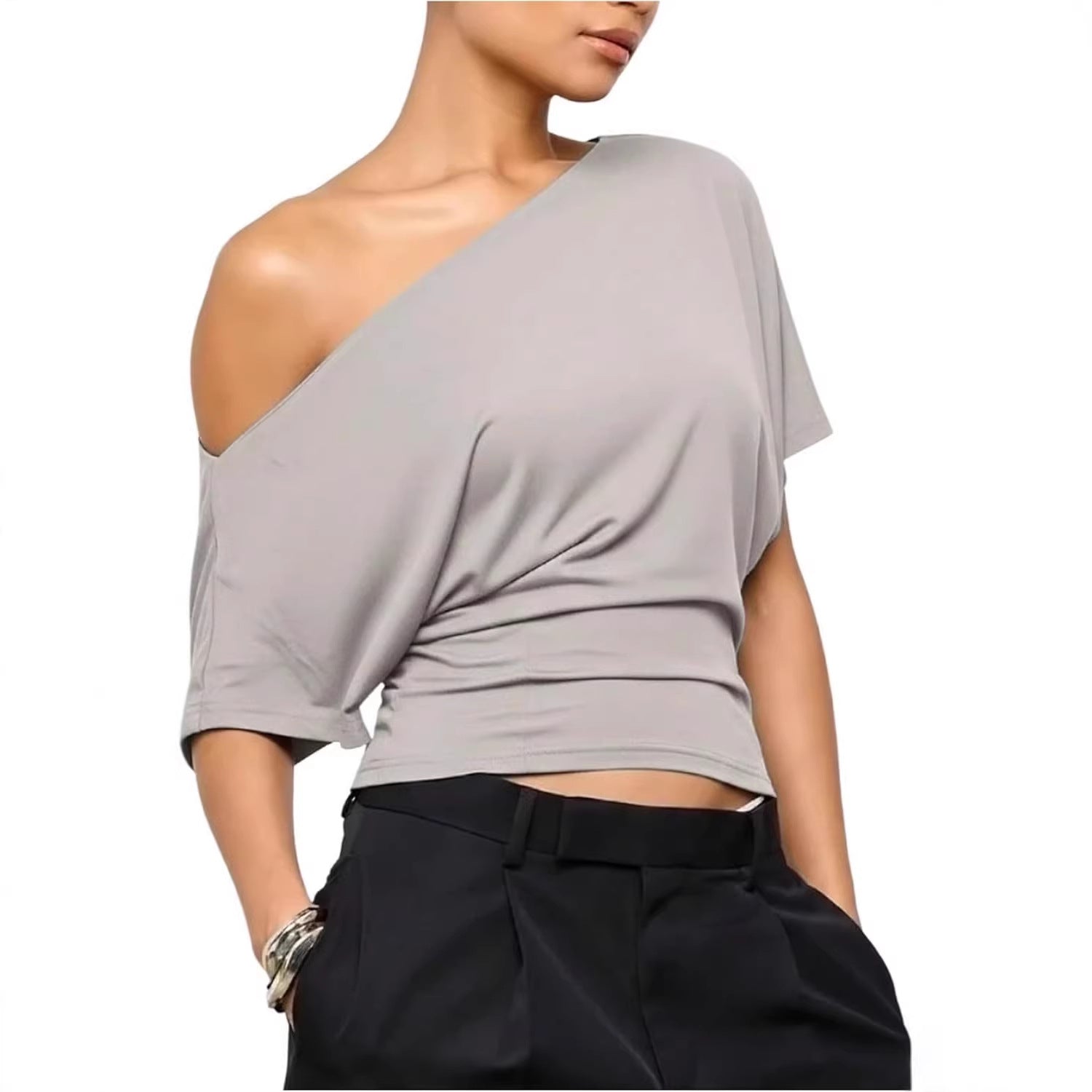 Woman wearing a gray one-shoulder top and black pants on a white background