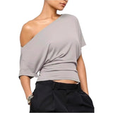 Woman wearing a gray one-shoulder top and black pants on a white background