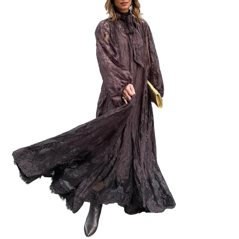 Woman wearing a long dark brown lace dress against a gray tiled wall.