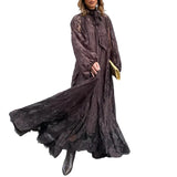 Woman wearing a long dark brown lace dress against a gray tiled wall.