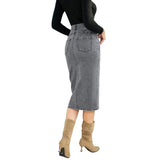 Person wearing a gray skirt and tan boots standing in front of a blue door and flowering plant.