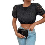 Person wearing a black lace top and blue jeans, holding a black handbag against a white wall.